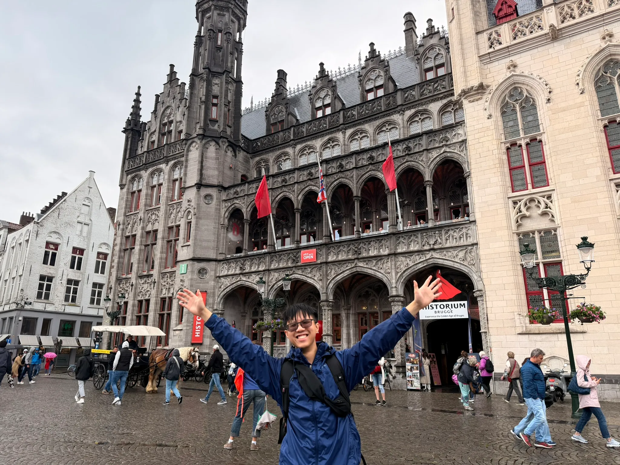 Sean with arms spread wide in front of the Historium on the Markt in Bruges, on a grey day